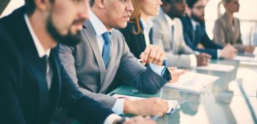 Pensive young businessman listening to explanations at seminar surrounded by other listeners